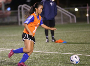 Guam U16 Women's national team head coach Brett Maluwelmeng (in background) watches as Hopemary Calip prepares to kick the ball toward the goal during a recent open tryout session for the team at the Guam Football Association National Training Center.