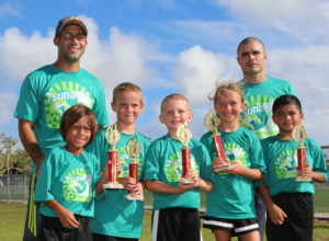 Tsunami team members pose with their championship trophies of the U8 division of the 4th Guam Football Association 3v3 Grassroots Tournament held Saturday at the GFA National Training Center. From left to right are: coach Jeff Garcia, Liam Leiser, Cameron Jarden, Jarrid Dame, Ella Liebhardt, coach Steve Moore, and Nicholas Moore. Tsunami defeated Wings Red in the final with the golden goal in extra time.